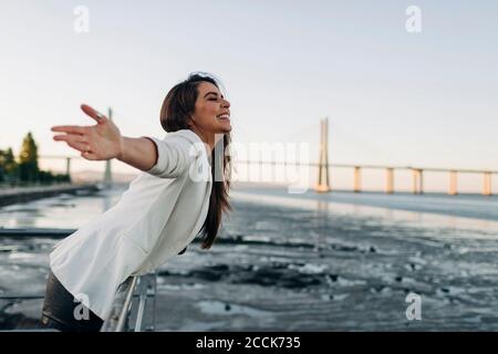 Young woman with open arms standing at riverside Stock Photo