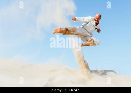 Mature man jumping while practicing karate on sand at beach against sky Stock Photo