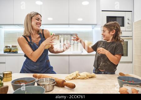 Cheerful mother and daughter playing with pizza dough in kitchen Stock Photo