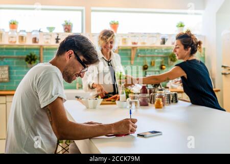 Man making notes while women in background at kitchen island in cooking school Stock Photo