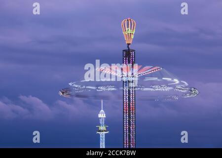 Germany, Bavaria, Munich, Aerial view of illuminated chain swing ride spinning against purple sky at dusk Stock Photo