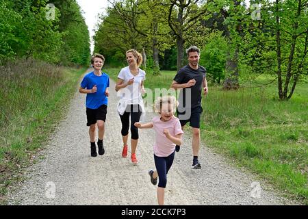 Children running with parents on dirt road amidst trees and plants in forest Stock Photo