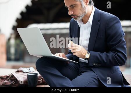 Businessman using laptop while eating food in city Stock Photo