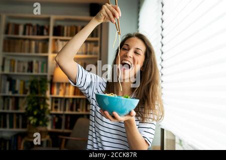 Young woman eating spaghetti while sitting by window at home Stock Photo