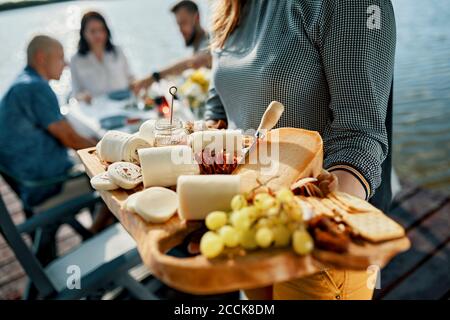 Friends having dinner with a cheese platter at a lake Stock Photo