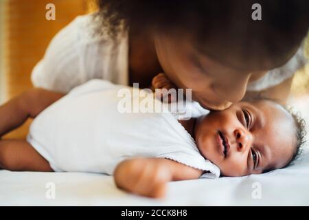 Close-up of mother kissing newborn daughter lying on bed at home