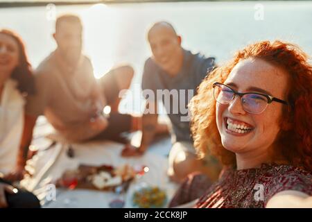 Happy redheaded woman having picnic with friends on jetty at a lake at sunset Stock Photo