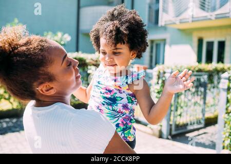 Close-up of mother carrying cute daughter while standing outdoors during sunny day Stock Photo