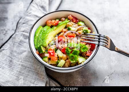Bowl of vegetarian quinoa salad with chick-peas, avocado, cucumber, tomato, onion and parsley Stock Photo
