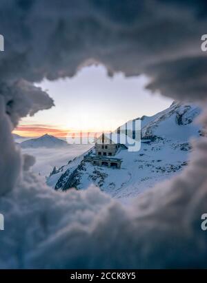 Secluded mountain hut seen through hole in snow Stock Photo