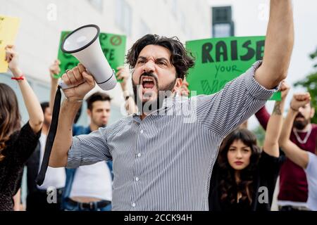 Man holding megaphone screaming with protestors on street Stock Photo