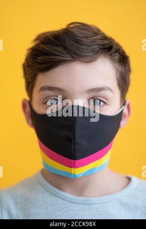Close-up of boy wearing multi colored mask against yellow background Stock Photo