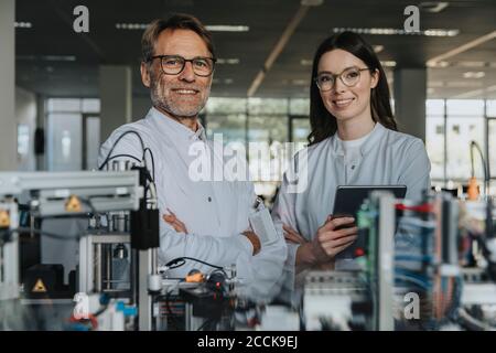 Smiling male and female scientists standing by machinery in laboratory Stock Photo