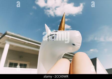 Close-up of mature woman with unicorn inflatable ring against blue sky during sunny day Stock Photo