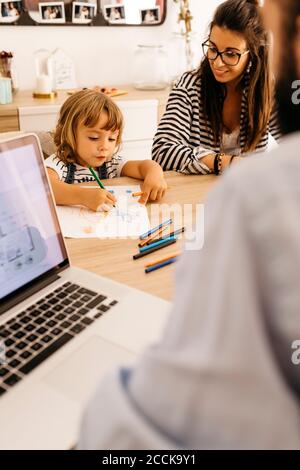 Cute girl painting on paper while sitting with parents in dining room Stock Photo