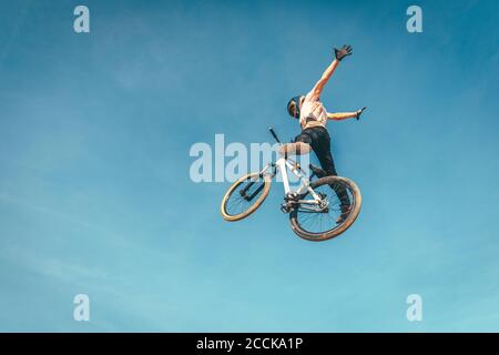 Carefree man performing stunt with bicycle against blue sky during sunset Stock Photo