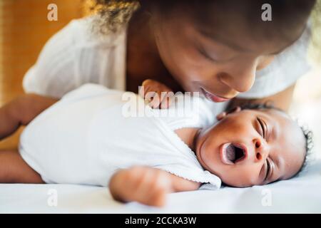 Close-up of mother looking at cute newborn daughter yawning while lying on bed Stock Photo