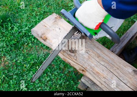 A man's gloved hand holds a chainsaw over a log. A man working a sawmill. Stock Photo