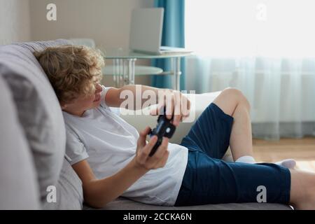playful teenager keen on video games, sit on sofa in living room holding console in hands, enjoy, spare time Stock Photo
