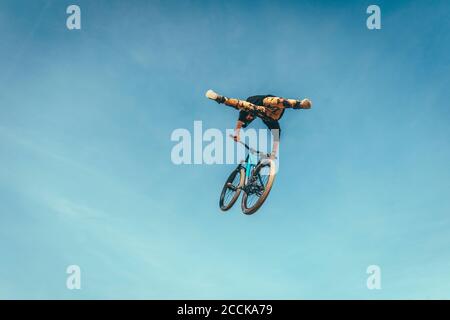 Young man performing stunt with bicycle against blue sky at park during sunset Stock Photo