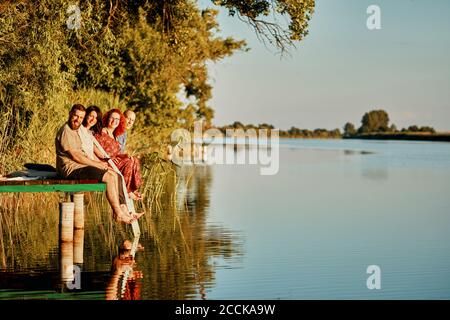 Portrait of smiling friends reflected in water sitting on jetty at a lake Stock Photo