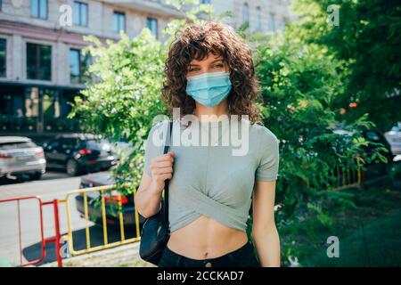Brunette curly woman wearing protective mask in city