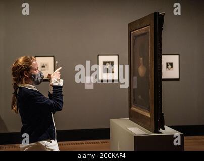 A woman wearing face covering takes a photograph of a painting by Aubrey Beardsley mounted on a free standing double face frame Stock Photo