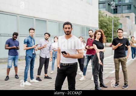 Group of friends using smart phones wile standing on footpath in city Stock Photo