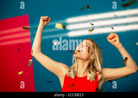 Cheerful young woman dancing amidst confetti in party Stock Photo