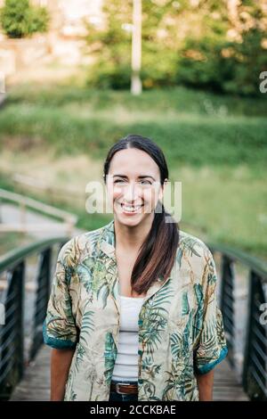Smiling woman standing over footbridge in public park Stock Photo