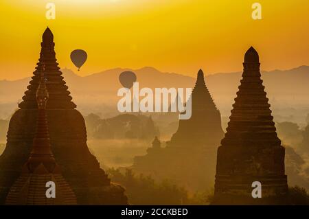 Myanmar, Mandalay Region, Bagan, Hot air balloons flying over ancient stupas at foggy dusk Stock Photo