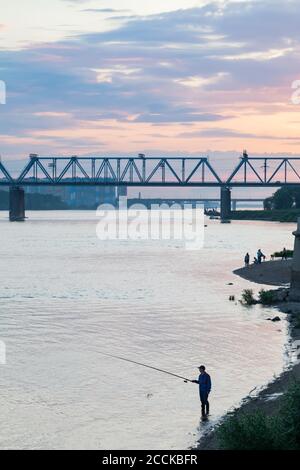 Novosibirsk, Russia - 07.12.20: Bank of the Ob river on the embankment, a fisherman is fishing at sunset in the evening. Stock Photo