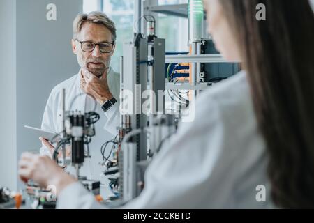 Thoughtful male scientist looking at machinery while working with female colleague in laboratory Stock Photo