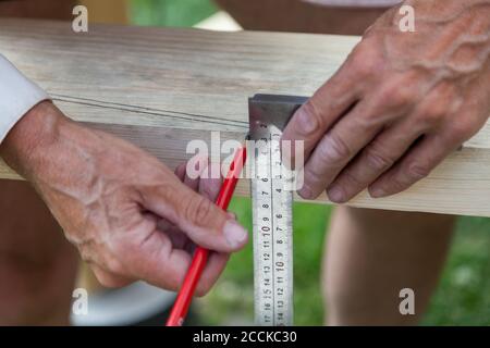Close-up of adult male hands holding woodworking marking tool - red pencil and metal ruler corner and measures and marks the area for processing on a Stock Photo