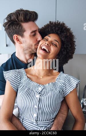 Loving man kissing cheerful woman in kitchen Stock Photo