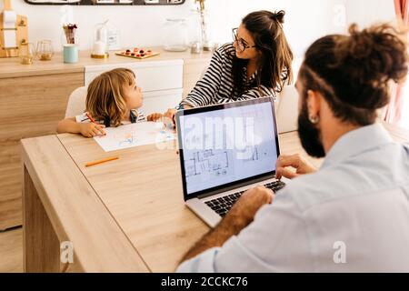 Man using laptop while mother and daughter painting in dining room Stock Photo