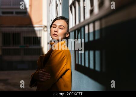 Young woman with eyes closed leaning on wall Stock Photo