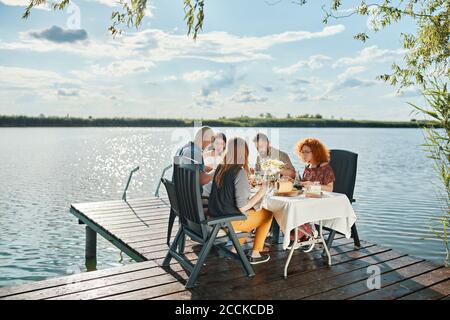 Friends having dinner on jetty at a lake Stock Photo