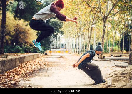 Male friends jumping in park during autumn Stock Photo