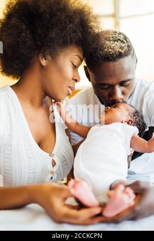 Close-up of man kissing newborn daughter held by mother at home
