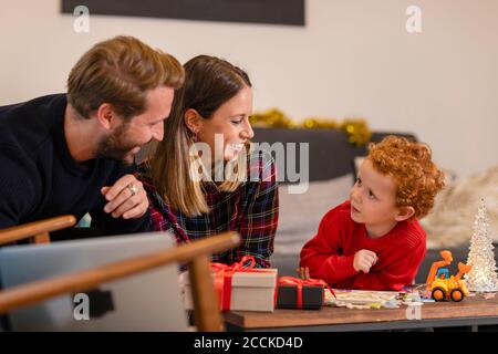 Smiling parents and son looking at each other in living room during Christmas Stock Photo