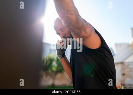 Confident mature man practicing boxing with punching bag against clear sky in yard