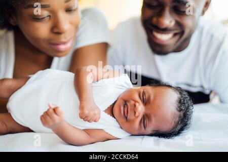Close-up of smiling parents looking at newborn daughter sleeping on bed