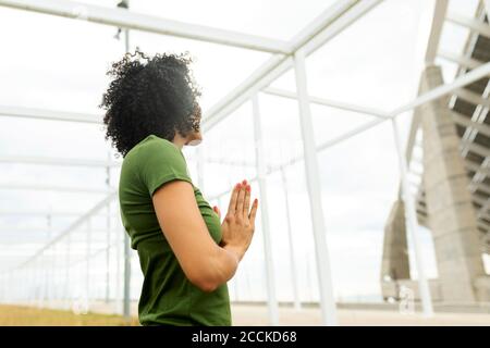 Mid adult woman meditating while standing against built structure in city