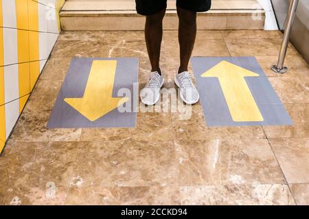 Legs of young man standing by arrow symbols on floor at subway station Stock Photo