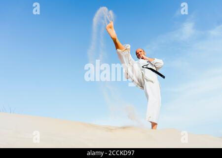 Mature man practicing karate on sand at beach against sky Stock Photo