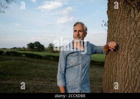 Content mature man leaning against a tree trunk in the countryside Stock Photo