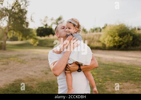 Father carrying and kissing little daughter on a meadow