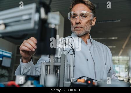 Male scientist with protective eyewear examining machine in laboratory Stock Photo