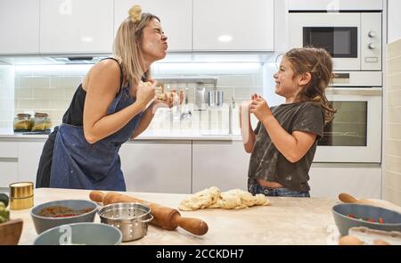 Mother and daughter playing with pizza dough in kitchen at home